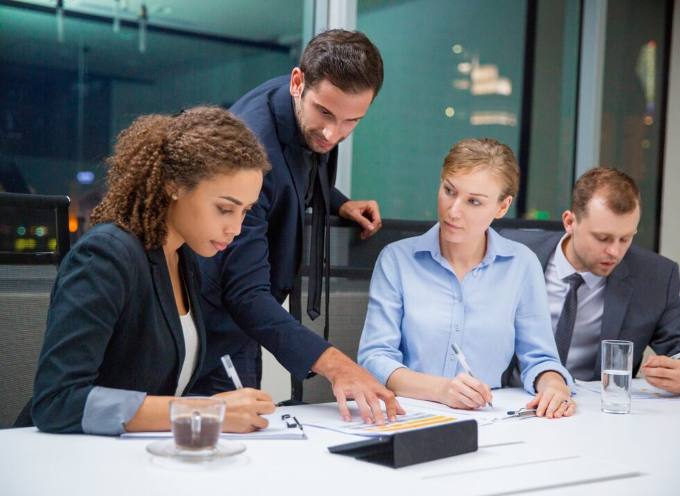 Business people sitting in conference room and discussing business issues. Executive manager standing, pointing to document and explaining his idea to business team